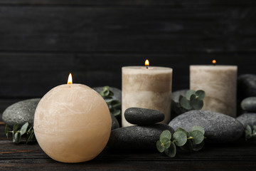 Composition with burning candles, spa stones and eucalyptus on dark wooden table