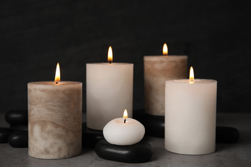 Fototapeta na wymiar Burning candles and spa stones on grey table