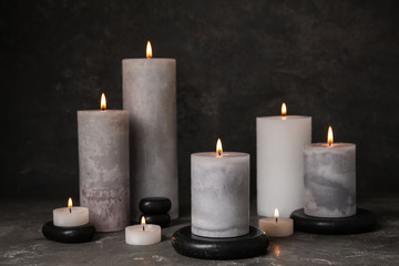 Burning candles and black spa stones on grey table