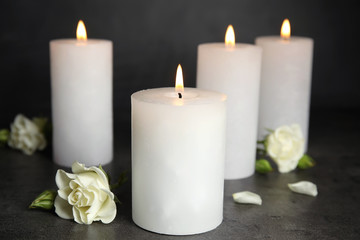 Fototapeta na wymiar Burning candles and flowers on dark grey table