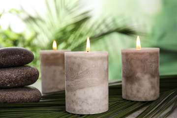Obraz na płótnie Canvas Burning candles and spa stones with palm leaf on table against blurred green background