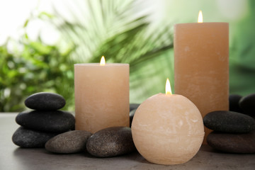 Fototapeta na wymiar Burning candles and spa stones on table against blurred green background