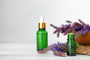 Bottles of sage essential oil and flowers on white table, space for text