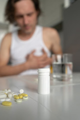 Pills and tablets lying on the table. A man holds his hands on his heart. Sickness, malaise, heartache. Foreground. Vertical. Close-up