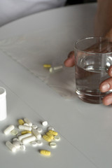 A man sits at the white kitchen table, on which there are tablets, pills, and holds a glass of water. Illness, malaise, cold, ache. Top-side view. Close-up. Vertical