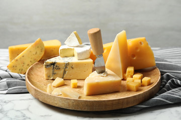 Wooden plate with different types of delicious cheese on marble table against light background