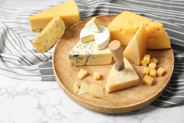 Different types of delicious cheese in wooden plate on marble table