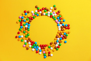 Frame made of delicious glazed candies on yellow background, top view. Space for text
