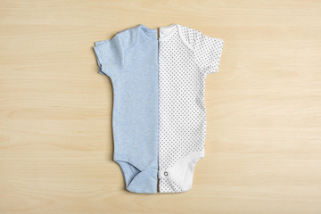 Different baby bodysuits on wooden background, top view