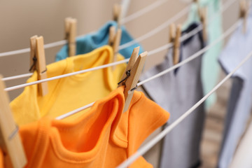 Different cute baby onesies hanging on clothes line against beige background, closeup. Laundry day
