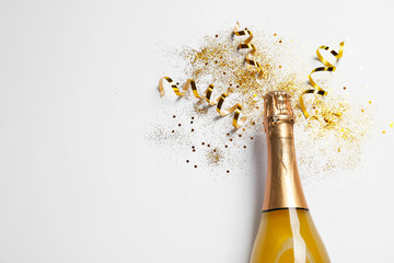 Bottle of champagne with gold glitter, confetti and space for text on white background, top view....