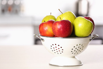 Colander with different sweet apples on table in kitchen, closeup. Space for text