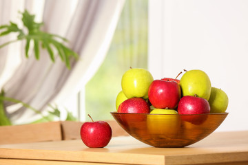 Bowl with different sweet apples on table in room, space for text
