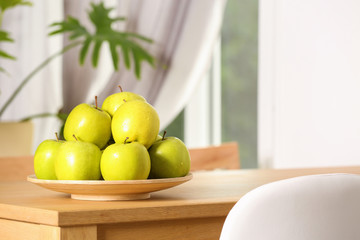 Plate with sweet green apples on table in room, space for text