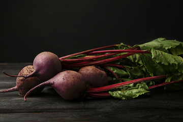 Fresh beets with leaves on dark wooden table against black background. Space for text