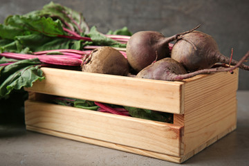 Wooden crate with fresh beets on table against grey background