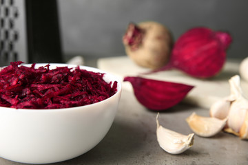 Bowl of grated fresh beets and garlic on table, closeup. Space for text