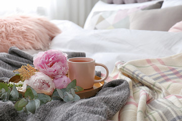 Fototapeta na wymiar Cup of drink and bouquet on bed with pillows in room