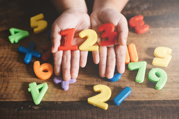 child hands showing a colorful 123 numbers agains wooden table. Concept of Child education, learning mathematics and counting - obrazy, fototapety, plakaty