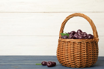 Fototapeta na wymiar Wicker basket of fresh acai berries on blue wooden table against white background, space for text