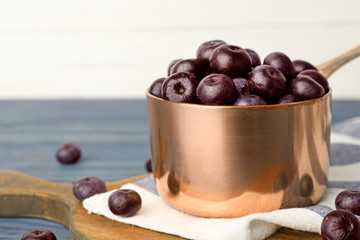 Metal saucepan of fresh acai berries on blue wooden table against white background, closeup. Space for text