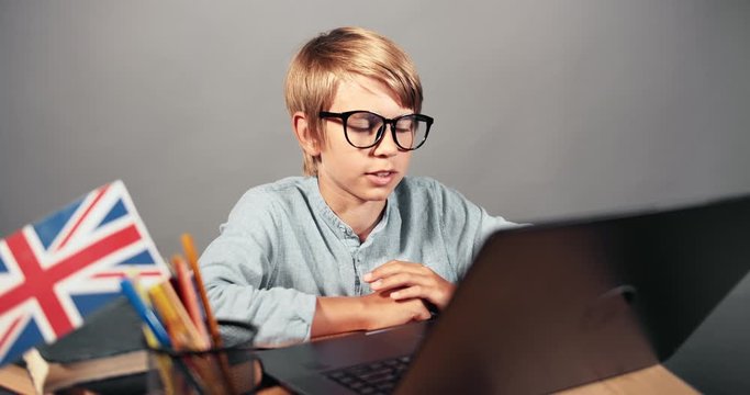 Smart teenage boy in eyeglasses having online english lesson on laptop, distant education