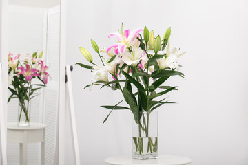 Fototapeta na wymiar Vase with bouquet of beautiful lilies on white table near mirror