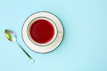 Cup of hibiscus tea with saucer and spoon on light blue background, flat lay. Space for text
