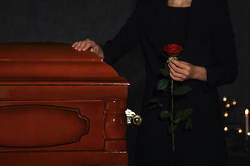 Young woman with red rose near casket in funeral home, closeup