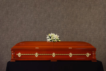 Wooden funeral casket with white lilies at grey wall - obrazy, fototapety, plakaty