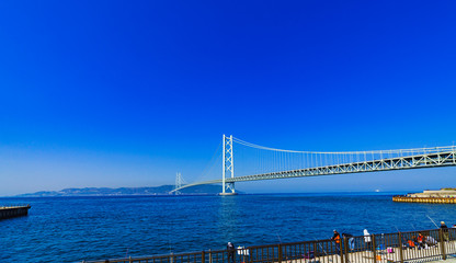[兵庫県の風景] 明石海峡大橋と淡路島を望む瀬戸内海の岸壁で早朝から家族で釣糸を垂らす釣り人達