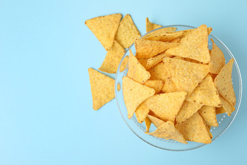 Glass bowl of tasty Mexican nachos chips on light blue background, top view