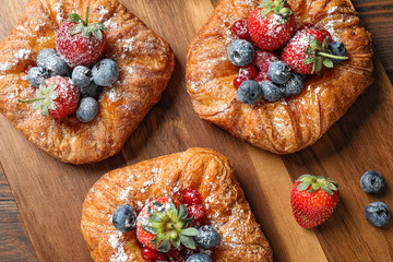 Fresh delicious puff pastry with sweet berries on wooden board, flat lay