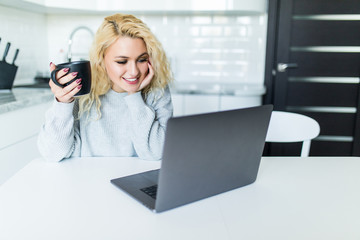 Young blonde woman using laptop in the kitchen at home