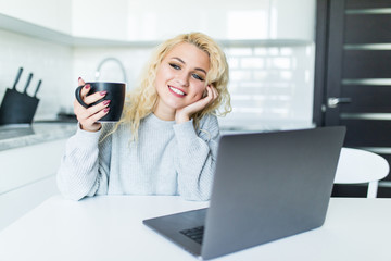 Happy young woman in the kitchen reading he news on her laptop