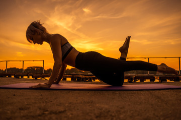 Woman exercising pilates in sunset. One legged ladies push up exercise. 