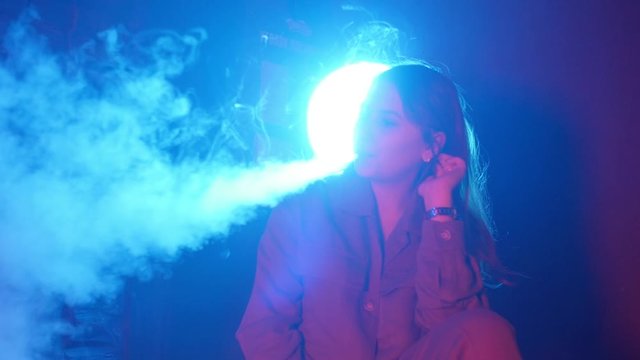 Young woman smoking vaporizer in Club on a colorful light