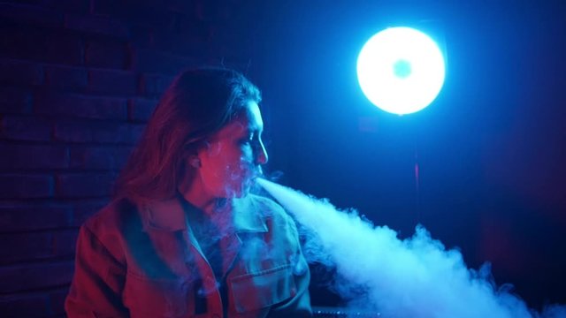 Young woman smoking vaporizer in Club on a colorful light