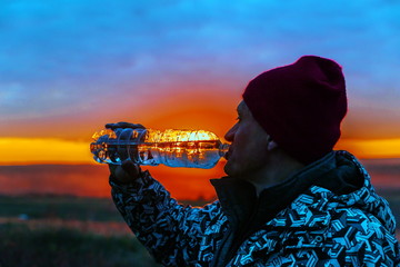 Handsome mature men drink clean spring water from a plastic bottle on the background of the sunset.