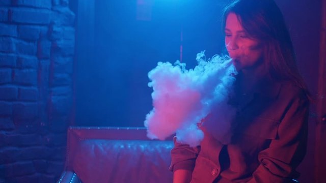 Young woman smoking vaporizer in Club on a colorful light