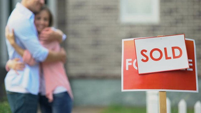 Sold sign with hugging young couple on background, private property, relocation