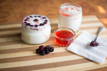Yogurt in transparent jars with fresh blackberry and strawberry voyen with a spoon, on wooden background