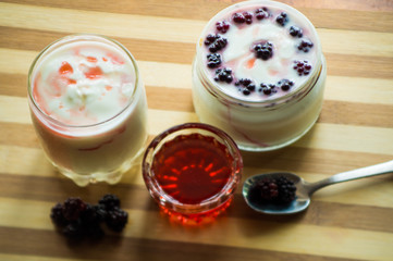 Yogurt in transparent jars with fresh blackberry and strawberry voyen with a spoon, on wooden background