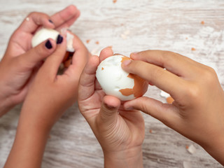 children's hands peeling a boiled egg on wooden background