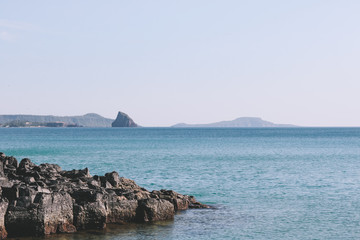 Rocky beach with calm blue sea and mountain, island far away. Shark fins rock in Phu Yen, Vietnam.