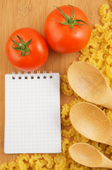 Recipe concept with macaroni, tomatoes, wooden spoons and notebook page