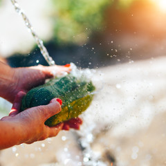 Washing vegetables, woman hands wash green zucchini outdoors sun light