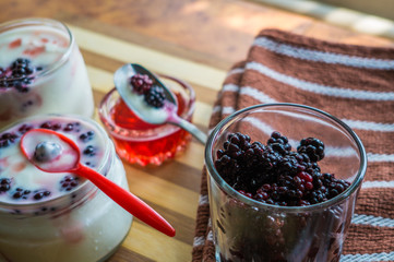 Yogurt in transparent jars with fresh blackberry and strawberry voyen with a spoon, on wooden background