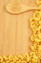 Raw macaroni with spoon on wooden background