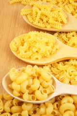 Raw macaroni with spoons on wooden background